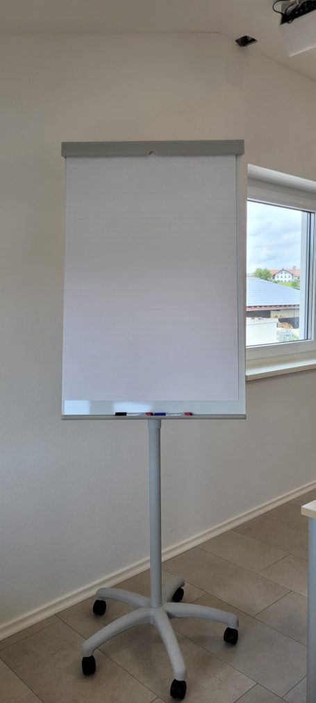 Ein leerer Flipchart-Ständer mit Rollen in einem hellen Raum.