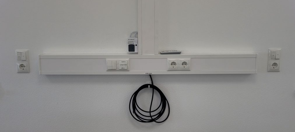 Weißes Wandpaneel mit Steckdosen und einem Kabel, das herunterhängt.