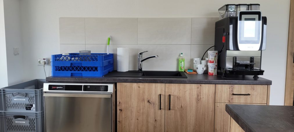 Küchenzeile mit Geschirrspüler, Kaffeemaschine und Spüle, blaue Kiste an der Wand.