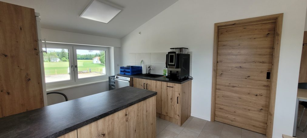 Küche mit Holzmöbeln, Fenster und Zugang zu einem Raum mit einer Tür.