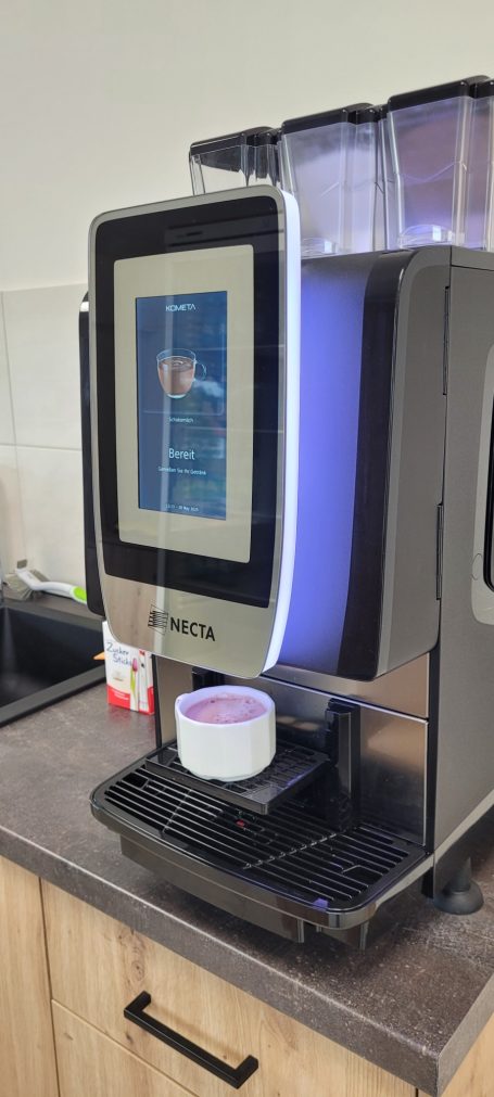 Kaffeebereiter mit digitalem Display und darunter einer Tasse auf der Ablage.