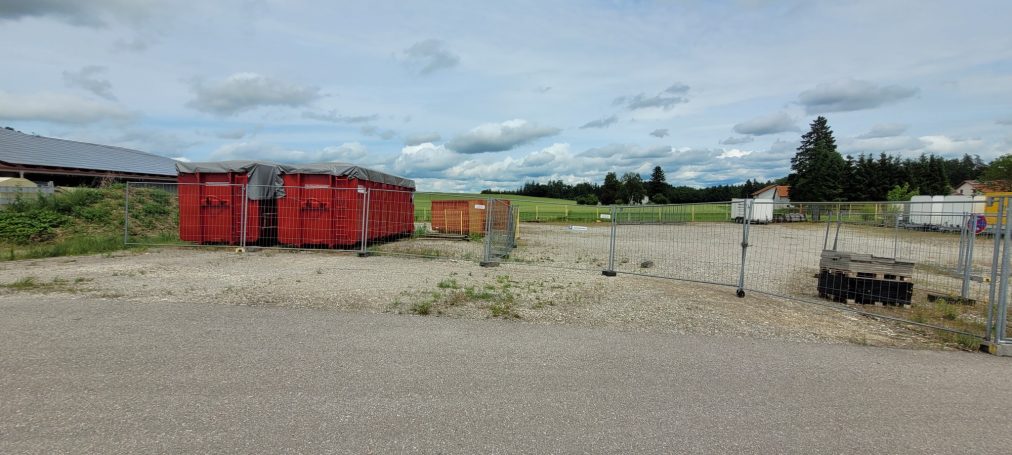 Blick auf einen Lagerplatz mit mehreren Containern und leerem Grundstück.